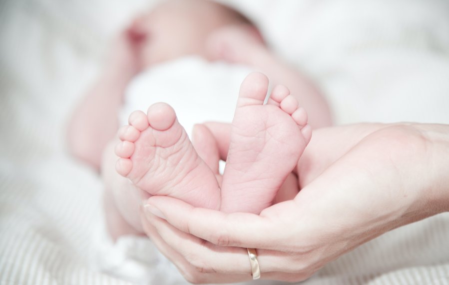 Nahaufnahme: Eine Hand hält die Füße eines liegenden Babys.
