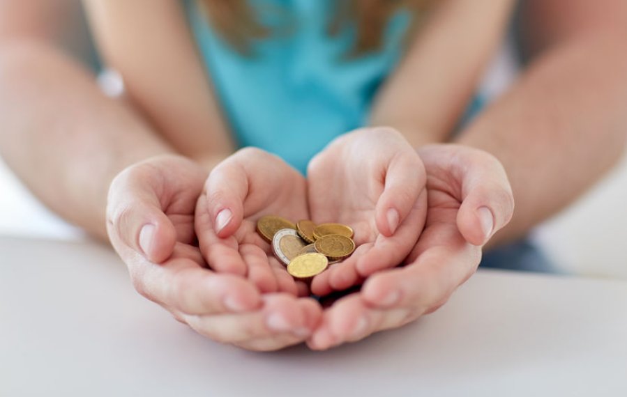 In den Händen einer erwachsenen Person liegen die Hände eines Kindes. In den Händen des Kindes liegen Euromünzen. 